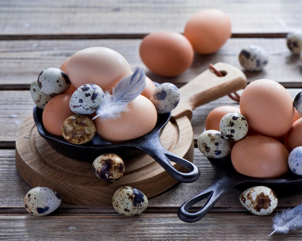 Перепелиные и куриные яйца на сковородке на столе
