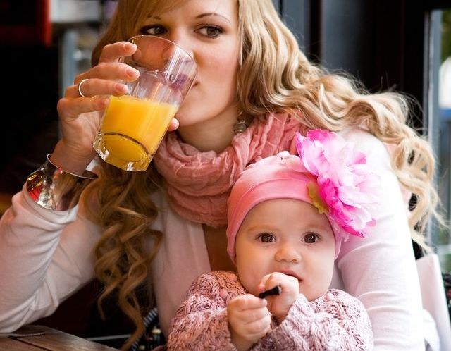 Женщина пьет сок из стакана с ребенком на руках