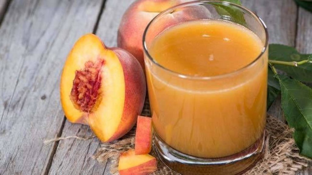 Персиковый сок в стакане и персики на деревянном столе