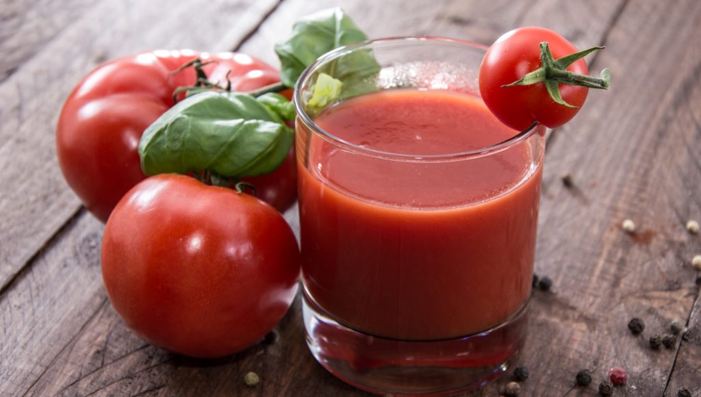 Томатный сок в стакане и помидоры на деревянном столе