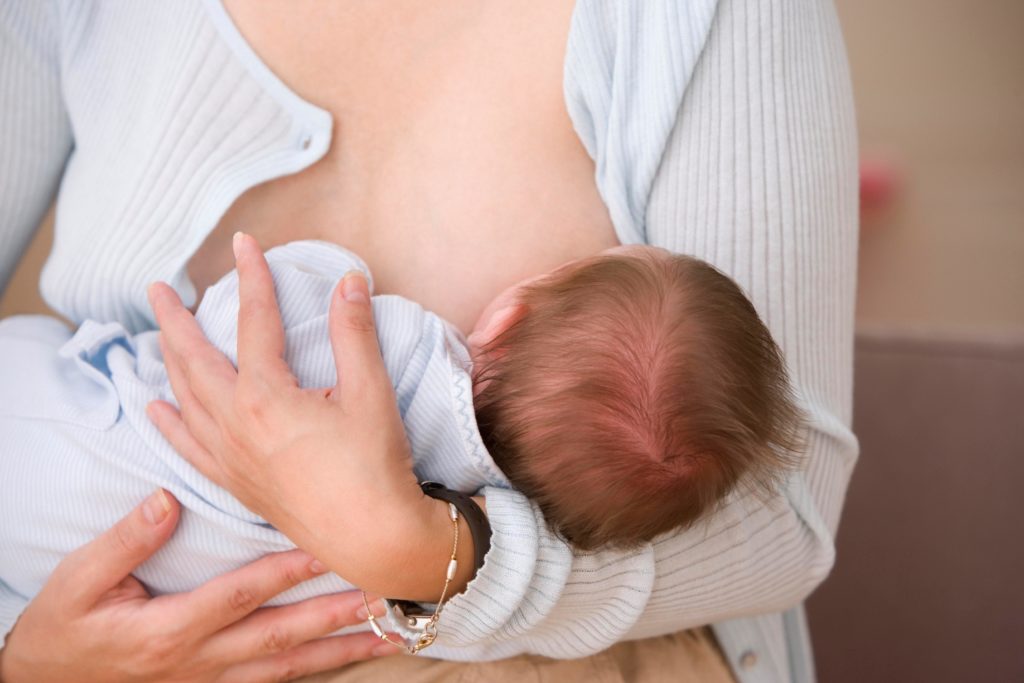 Младенец сосет грудь на руках у мамы