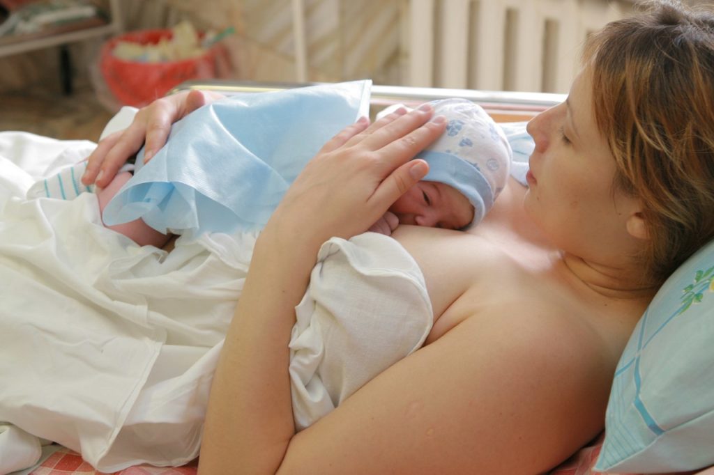 Молодая мама крмит новорожденного грудью после родов