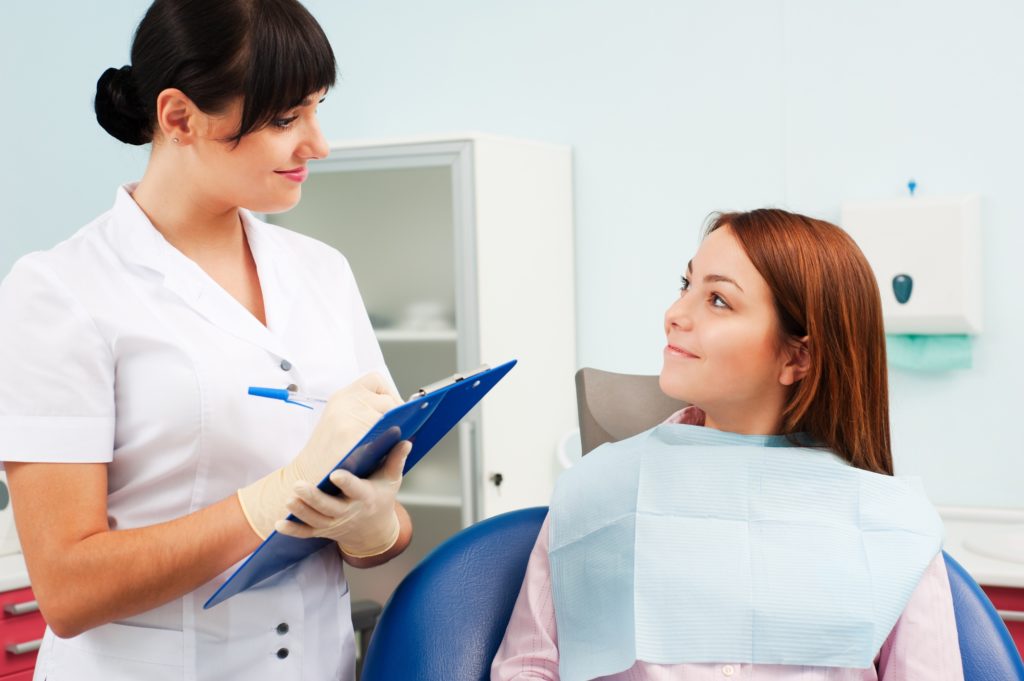 Девушка сидит в стоматологическом кресле и смотрит на стоматолога