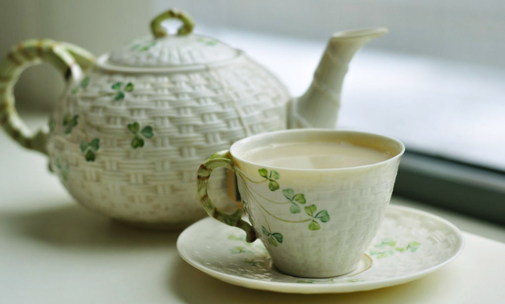 Зеленый чай с молоком в чашке на столе, заварочный чайник на заднем фоне
