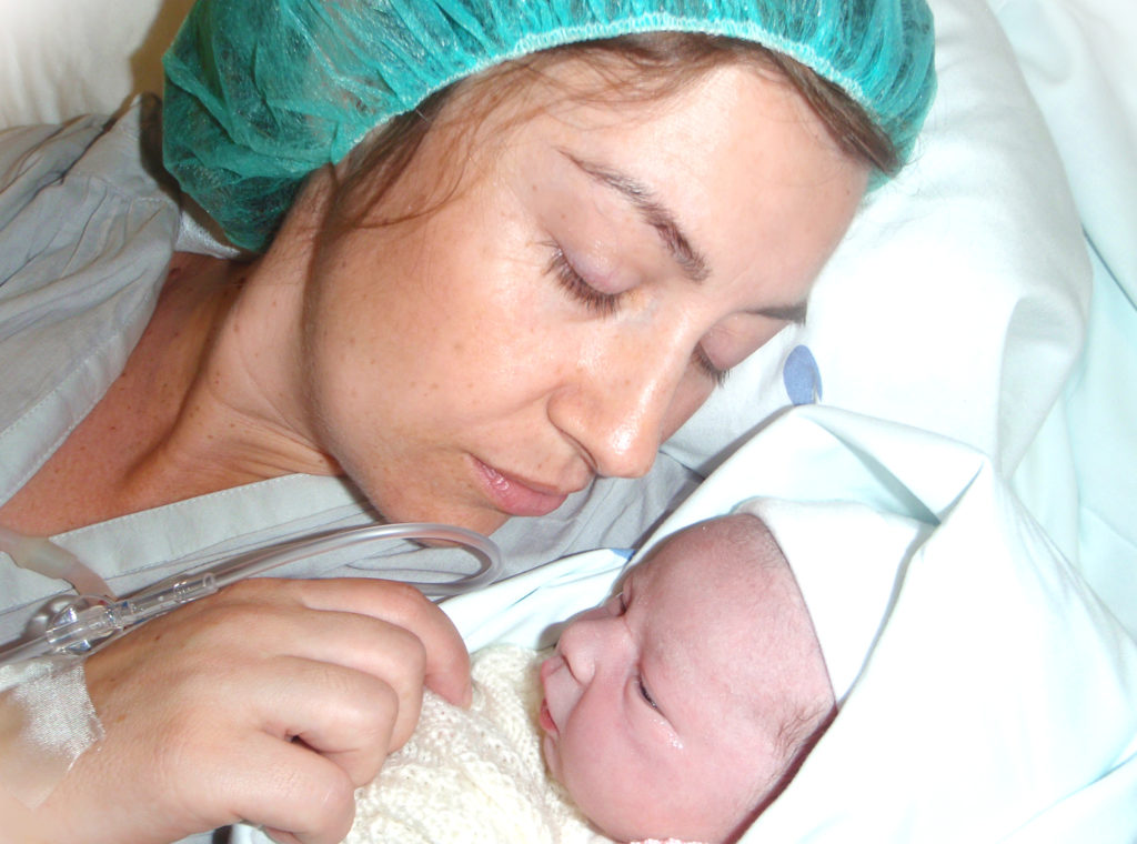 Мама с новорожденным лежат в больнице на кровати
