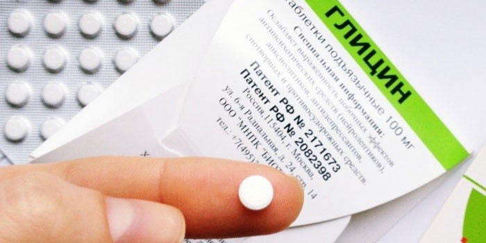 Таблетка глицина на пальце на фоне упаковки таблеток